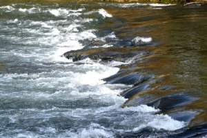 Wasser fliesst in einem Fluss über ein Schwelle